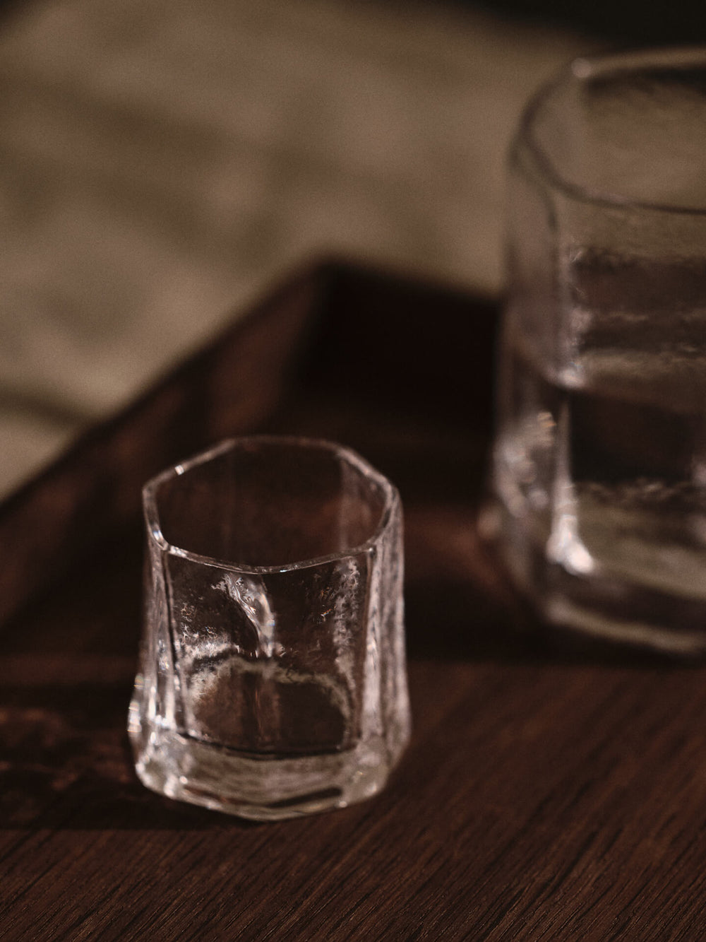 Två klara glas med strukturerade, fasetterade sidor på ett mörkt bord, ett fyllt med vatten