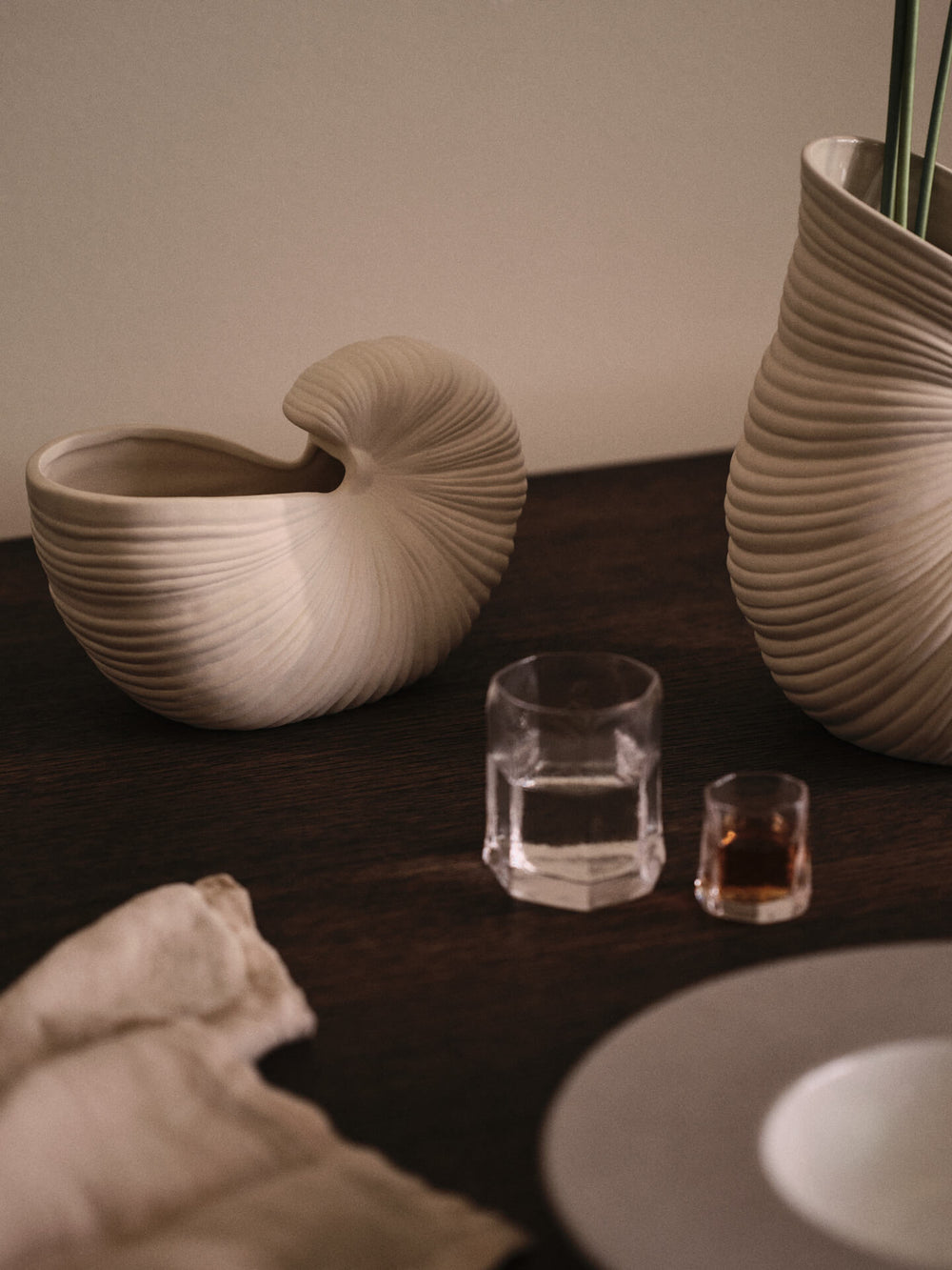 Två fasetterade glas på ett mörkt bord med snäckformade vaser och en vikt duk