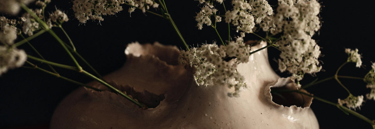 Det lilla extra, närbild på en off-white vas med rivna, ojämna öppningar med kvistar av små vita blommor