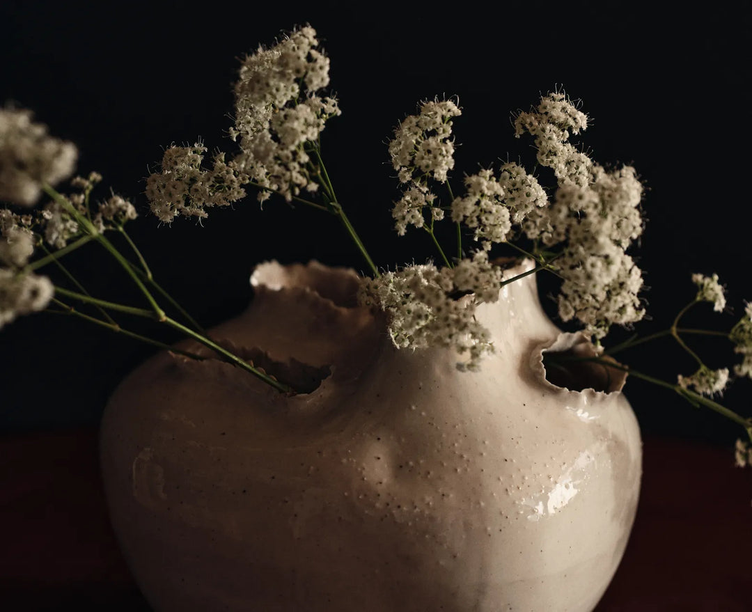 Det lilla extra, närbild på en off-white vas med rivna, ojämna öppningar med kvistar av små vita blommor
