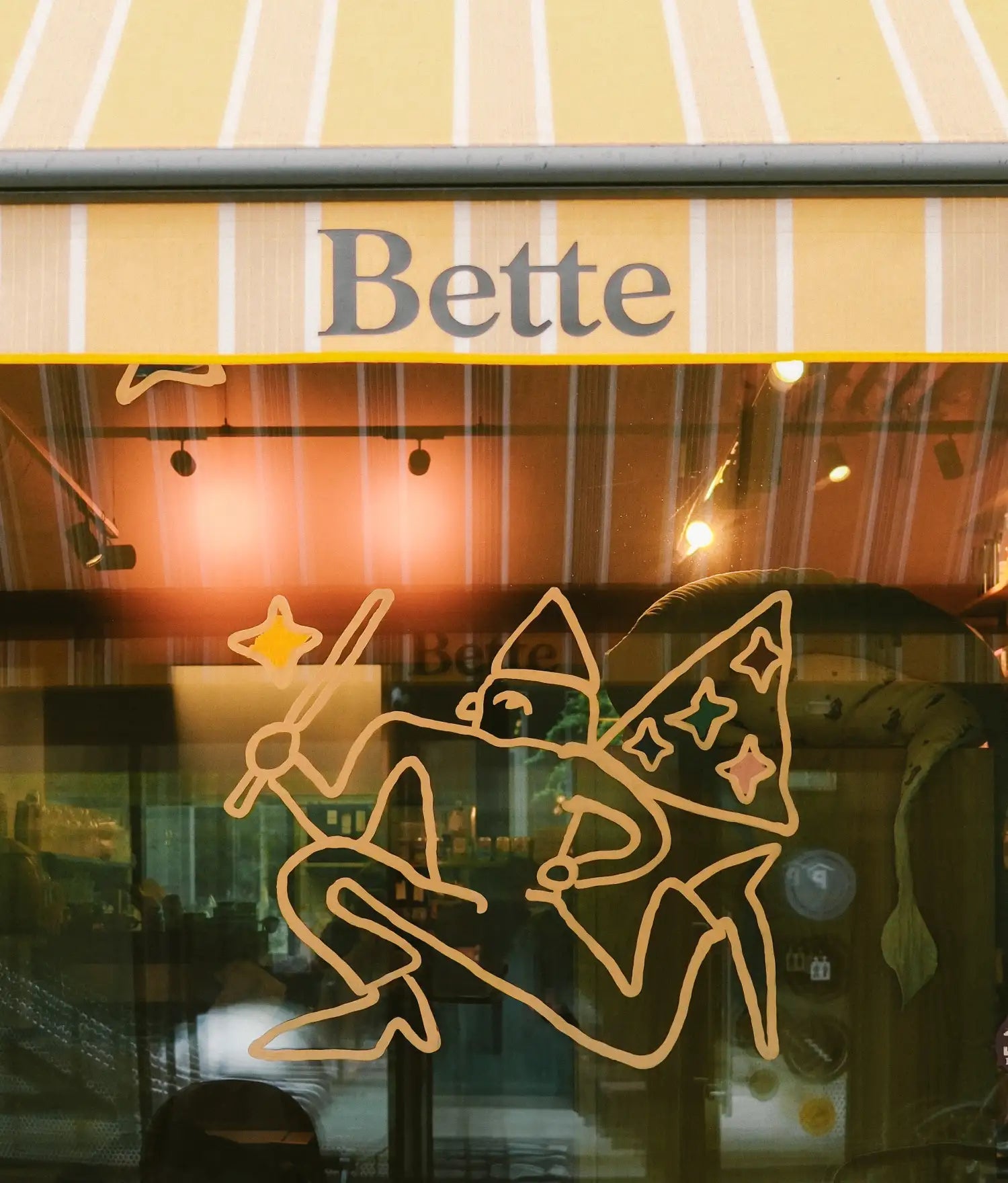 Skyltfönster med randig markis där det står Bette, linjeteckning av en älva på glaset
