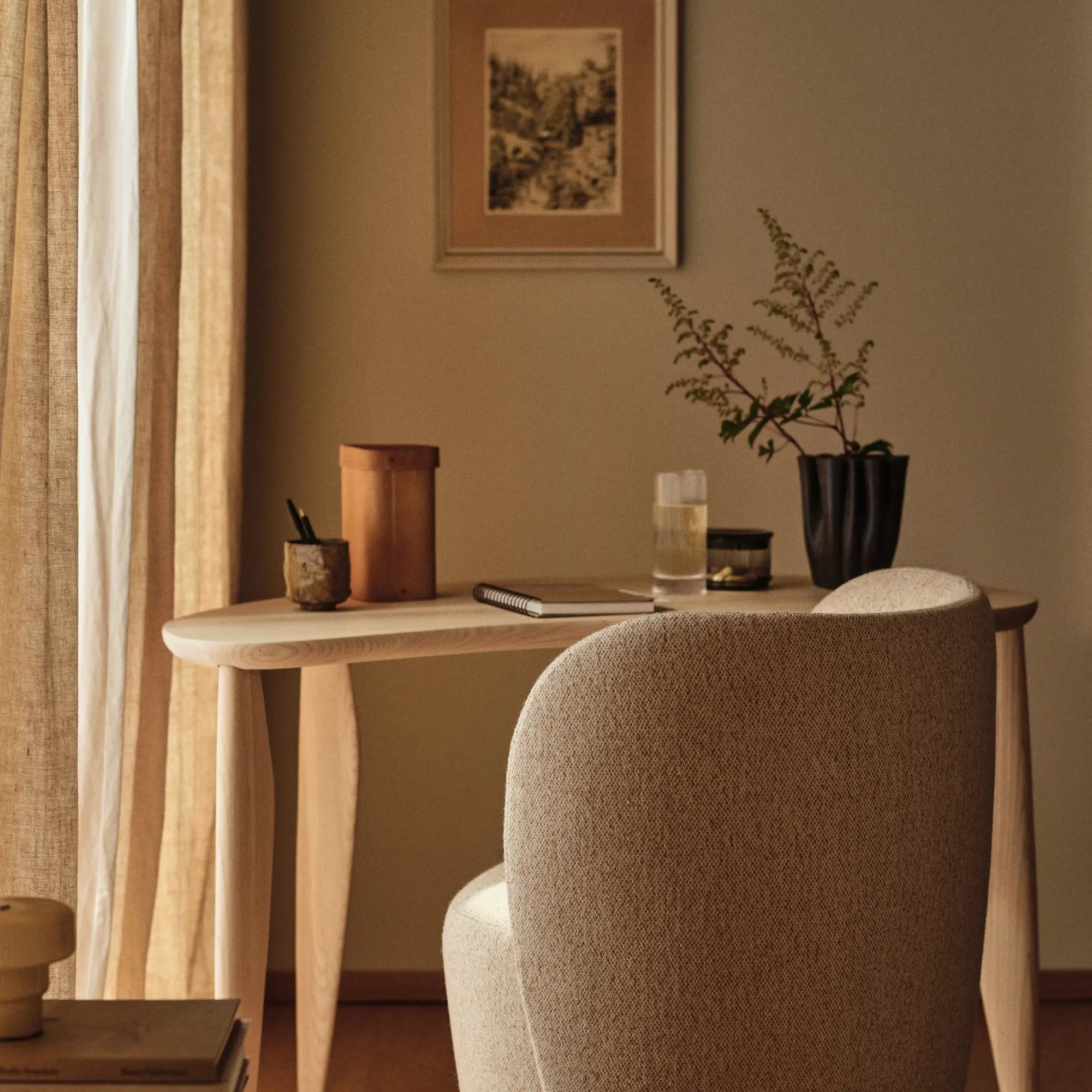 Smalt konsolskrivbord vid ett fönster med gardin, med anteckningsbok, vas och stoppad stol